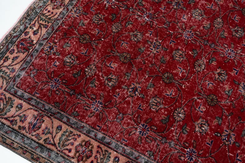 K&ouml;nnte beinhalten: Ausschnitt eines roten, im Used-Look gehaltenen Teppichs mit einem komplizierten Blumenmuster. Der Teppich hat ein verblasstes Aussehen, mit einem Rand, der ein helleres, florales Design aufweist. Die Farbpalette umfasst Rot-, Braun-, Blau- und Beiget&ouml;ne.