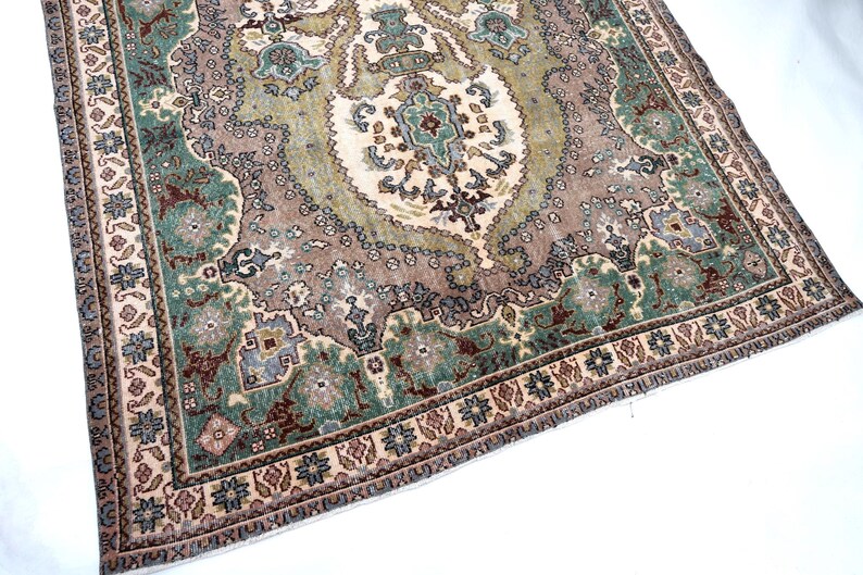May include: A rectangular area rug featuring a central medallion design in shades of sage green, dusty rose, and cream. The rug displays an intricate floral and geometric pattern with a wide border containing repeating motifs in blue, brown, and tan.