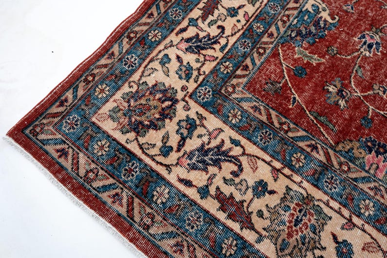 May include: Close-up of a section of a vintage rug with a detailed floral pattern. The rug features a red field with a cream-colored border and blue accents. The design includes stylized flowers and leaves.