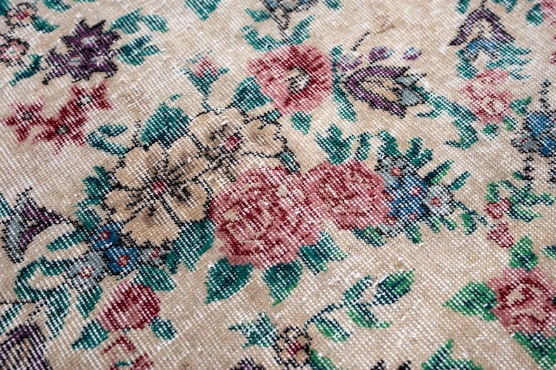 Pode incluir: Close-up de um tapete floral bege com aspecto envelhecido. O tapete apresenta um padr&atilde;o de flores vermelhas, rosa, roxas, azuis e bege com folhas verdes. O tapete tem uma est&eacute;tica vintage e antiga.