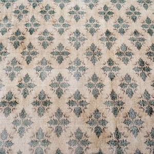 May include: A rectangular area rug featuring a repeating diamond-shaped floral pattern in dark green against a light beige background. The rug is framed by a solid dark green border that runs along the edges, creating a distinct contrast.