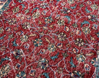 May include: Close-up of a vintage rug with a distressed, floral pattern. The rug features a deep red field with teal, beige, and blue accents. The border is teal and beige. The rug's design is intricate and detailed.
