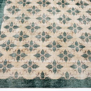 May include: A rectangular area rug featuring a repeating pattern of dark teal floral motifs set against a light beige background. The rug is framed by a solid dark teal border that runs along the edges, creating a distinct contrast in color.