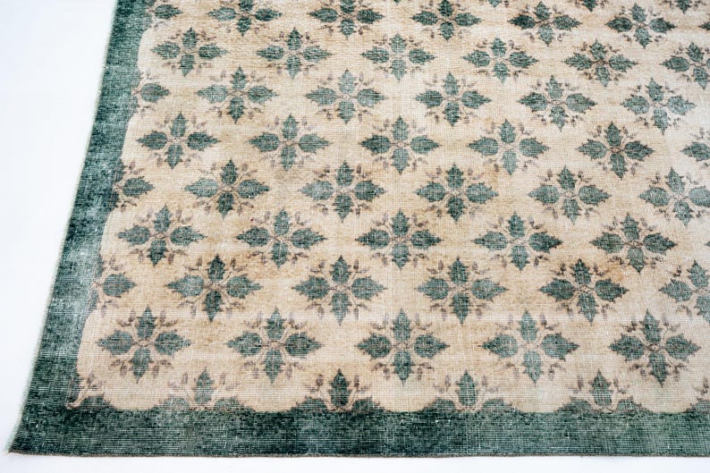 May include: A rectangular area rug featuring a repeating pattern of dark teal floral motifs set against a light beige background. The rug is framed by a solid dark teal border that runs along the edges, creating a distinct contrast in color.