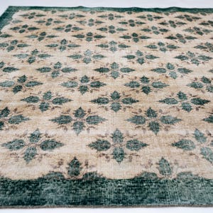 May include: A rectangular area rug featuring a repeating pattern of dark teal floral motifs set against a light beige background. The rug is framed by a wide, solid dark teal border that runs along the edges, creating a distinct contrast.
