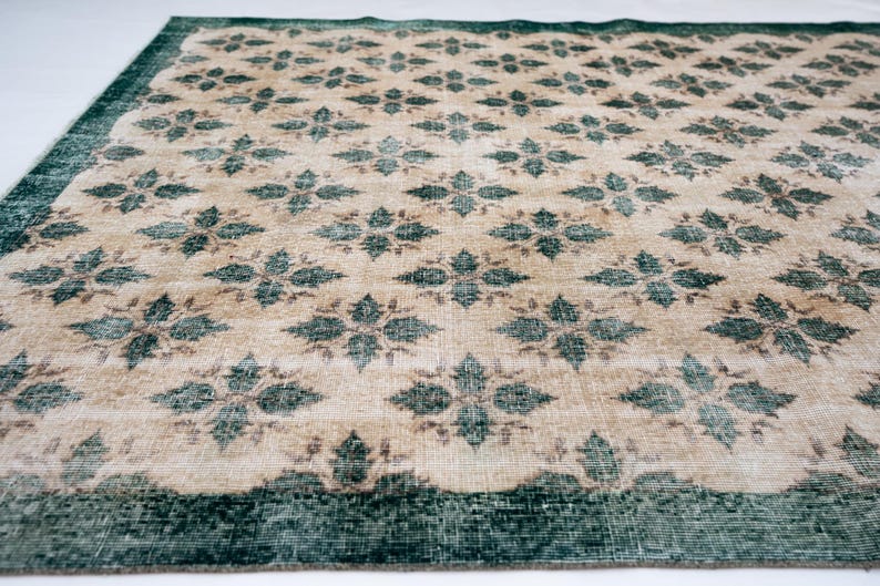 May include: A rectangular area rug featuring a repeating pattern of dark teal floral motifs set against a light beige background. The rug is framed by a wide, solid dark teal border that runs along the edges, creating a distinct contrast.