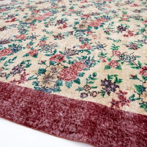 Pode incluir: Um tapete com padr&atilde;o floral com fundo creme e borda vermelha escura. O tapete apresenta um padr&atilde;o denso de flores rosa, azuis e roxas com folhas verdes. O design do tapete &eacute; detalhado e intrincado.