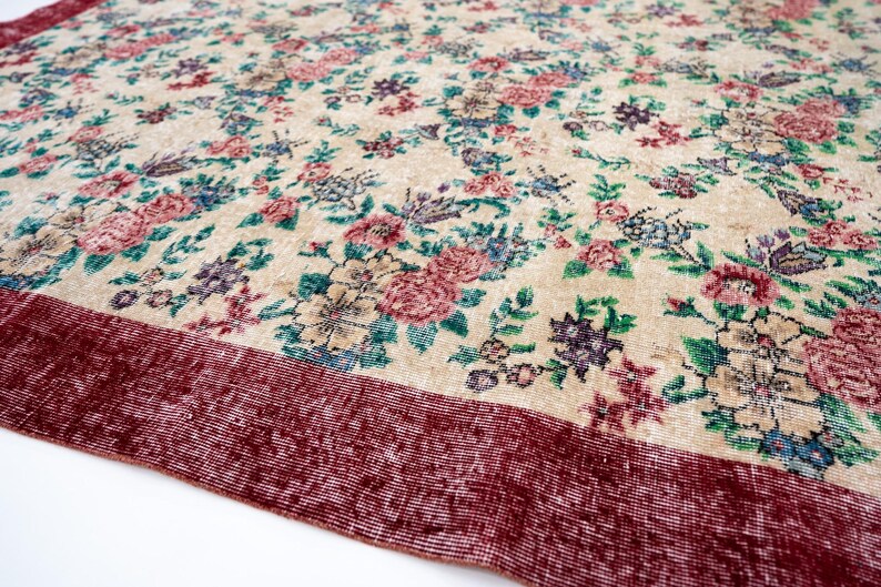 Pode incluir: Um tapete com padr&atilde;o floral com fundo creme e borda vermelha escura. O tapete apresenta um padr&atilde;o denso de flores rosa, azuis e roxas com folhas verdes. O design do tapete &eacute; detalhado e intrincado.