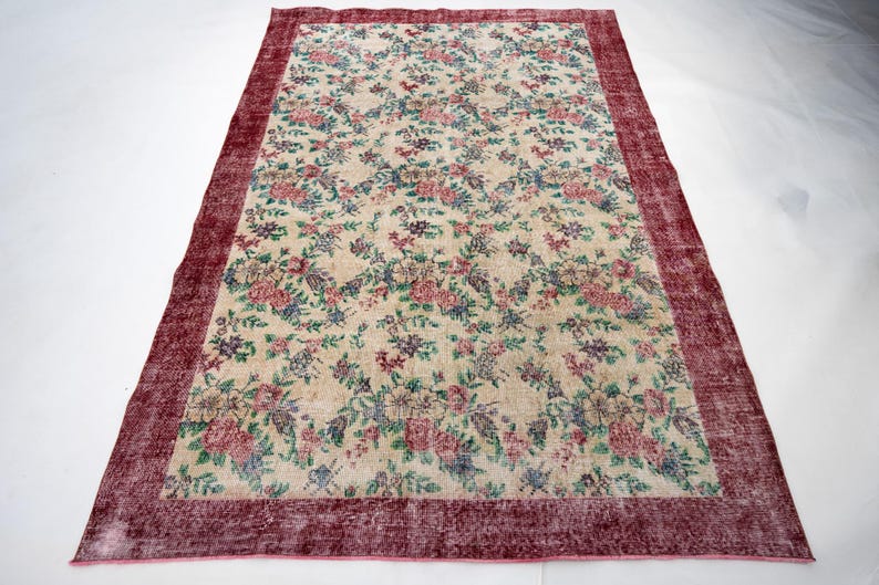 May include: Rectangular floral rug with a cream-colored background and a burgundy border. The rug features a pattern of pink, blue, and purple flowers and green leaves. The rug is a large size.