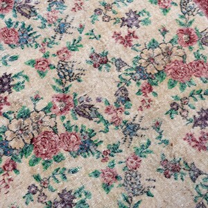 Pode incluir: Um tapete floral vintage com fundo creme e um padr&atilde;o de flores rosa, roxas e azuis com folhas verdes. O tapete tem uma borda bord&ocirc;.
