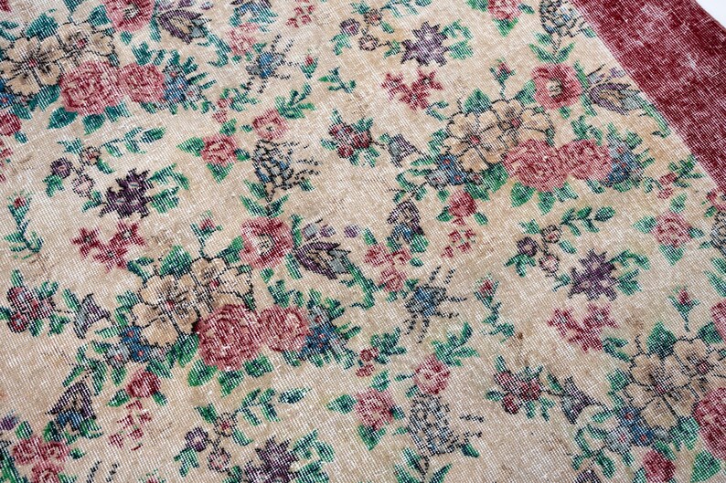 Pode incluir: Um tapete floral vintage com fundo creme e um padr&atilde;o de flores rosa, roxas e azuis com folhas verdes. O tapete tem uma borda bord&ocirc;.