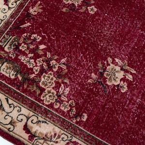 May include: Close-up of a section of a vintage red rug with floral patterns. The rug features a deep red field with faded areas and beige borders with intricate designs. Beige and brown floral motifs are scattered across the rug.