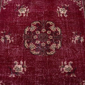 May include: A rectangular, vintage-style rug with a deep red background. The rug features a central medallion design and floral patterns in beige and brown. The border has a repeating floral and geometric pattern.