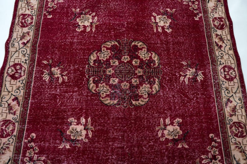 May include: A rectangular, vintage-style rug with a deep red background. The rug features a central medallion design and floral patterns in beige and brown. The border has a repeating floral and geometric pattern.