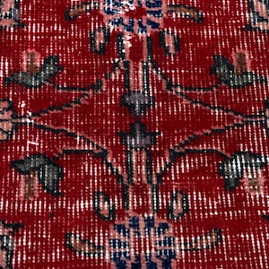 K&ouml;nnte beinhalten: Nahaufnahme eines roten Teppichs mit einem komplizierten Blumenmuster. Das Design zeigt stilisierte Blumen in Blau-, Grau- und Rosat&ouml;nen vor einem tiefroten Hintergrund. Der Teppich hat ein abgenutztes, Vintage-Aussehen.