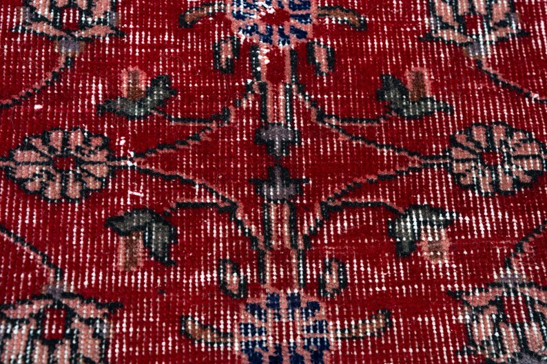 K&ouml;nnte beinhalten: Nahaufnahme eines roten Teppichs mit einem komplizierten Blumenmuster. Das Design zeigt stilisierte Blumen in Blau-, Grau- und Rosat&ouml;nen vor einem tiefroten Hintergrund. Der Teppich hat ein abgenutztes, Vintage-Aussehen.