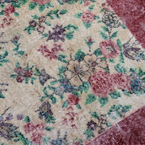 Pode incluir: Um tapete vintage com um padr&atilde;o floral em tons de bege, vermelho, verde, azul e roxo. O tapete tem um aspeto envelhecido, com uma borda bord&ocirc;. O design floral inclui rosas e outras flores.