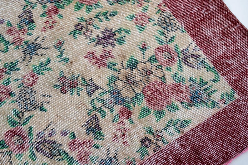 Pode incluir: Um tapete vintage com um padr&atilde;o floral em tons de bege, vermelho, verde, azul e roxo. O tapete tem um aspeto envelhecido, com uma borda bord&ocirc;. O design floral inclui rosas e outras flores.