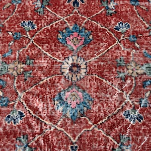 May include: Close-up of a red vintage rug with an intricate floral pattern. The design features blue, pink, and beige floral motifs on a red background. The rug has a distressed, aged appearance.