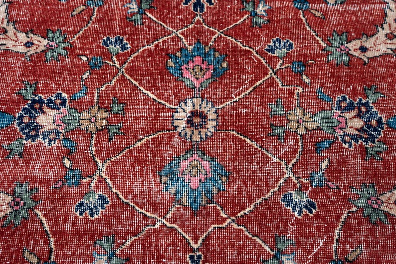 May include: Close-up of a red vintage rug with an intricate floral pattern. The design features blue, pink, and beige floral motifs on a red background. The rug has a distressed, aged appearance.