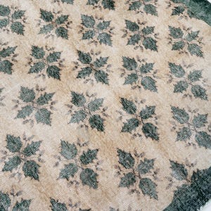 May include: A rectangular area rug featuring a repeating pattern of dark green, four-leaf floral motifs set against a light beige background. The rug has a wide, solid dark green border along the edge, showcasing a woven texture throughout the surface.