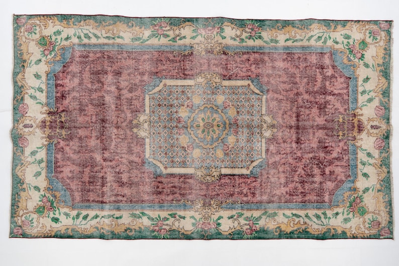 May include: Rectangular area rug with a distressed, vintage look. The rug features a central maroon field, framed by a light blue border and a cream-colored floral border. The rug's design includes floral and geometric patterns.