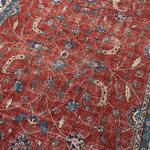 May include: A distressed, vintage-style rug with a rich red background. The rug features a detailed floral pattern in shades of blue, beige, and cream. The border has a complementary design. This rug is suitable for living rooms and bedrooms.