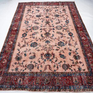 Pu&ograve; includere: Un tappeto rettangolare in stile vintage, con un campo centrale color pesca ornato da motivi floreali blu e turchese. Il bordo &egrave; rosso intenso con disegni intricati. Il tappeto, probabilmente in lana, &egrave; adatto per un soggiorno o una camera da letto.