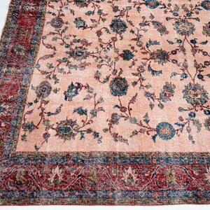 Pu&ograve; includere: Un grande tappeto rettangolare con un'estetica vintage sbiadita. Il tappeto presenta un campo centrale color pesca con un motivo floreale nei toni del blu, verde e marrone. Un bordo dettagliato in rosso e blu incornicia il design, aggiungendo un tocco classico.