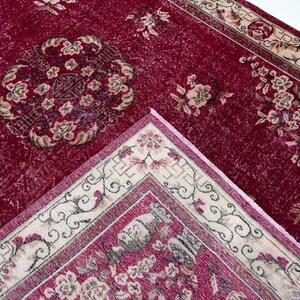 May include: A close-up of a red vintage rug with floral patterns. The rug has a central medallion design and a cream-colored border with floral and scroll motifs. The rug is made of a soft, textured material.