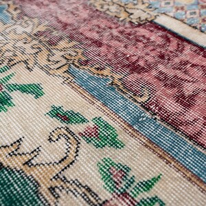 May include: Close-up of a section of a vintage rug with a patchwork design. The rug features floral and geometric patterns in shades of cream, burgundy, green, and blue. The texture is visible, showing the woven construction of the rug.