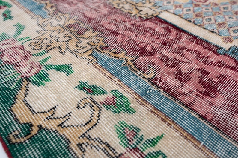 May include: Close-up of a section of a vintage rug with a patchwork design. The rug features floral and geometric patterns in shades of cream, burgundy, green, and blue. The texture is visible, showing the woven construction of the rug.