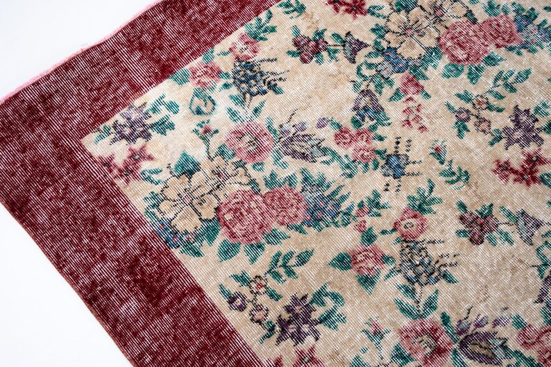 Pode incluir: Um tapete de estilo vintage com um campo central creme, adornado com um padr&atilde;o floral em tons de rosa, azul e roxo. O tapete tem uma borda bord&ocirc; escura, adicionando uma moldura contrastante ao design. Adequado para decora&ccedil;&atilde;o de casa.