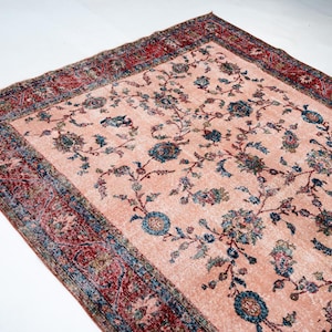 Pu&ograve; includere: Un tappeto rettangolare in stile vintage con sfondo color pesca chiaro e motivo floreale nei toni del blu, verde e marrone. Il bordo &egrave; rosso scuro con disegni intricati. Il tappeto &egrave; probabilmente in lana.