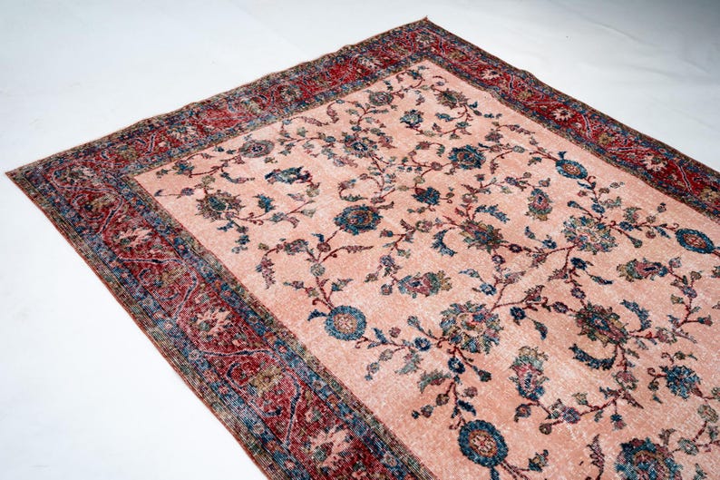 Pu&ograve; includere: Un tappeto rettangolare in stile vintage con sfondo color pesca chiaro e motivo floreale nei toni del blu, verde e marrone. Il bordo &egrave; rosso scuro con disegni intricati. Il tappeto &egrave; probabilmente in lana.
