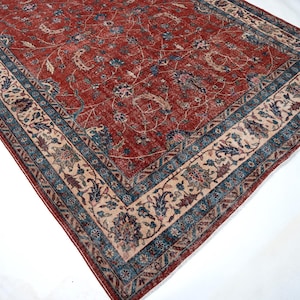 May include: A rectangular, antique-style rug with a red central field and intricate floral patterns. The rug features a border with blue and beige accents, creating a classic and elegant design. The rug's dimensions are not visible.