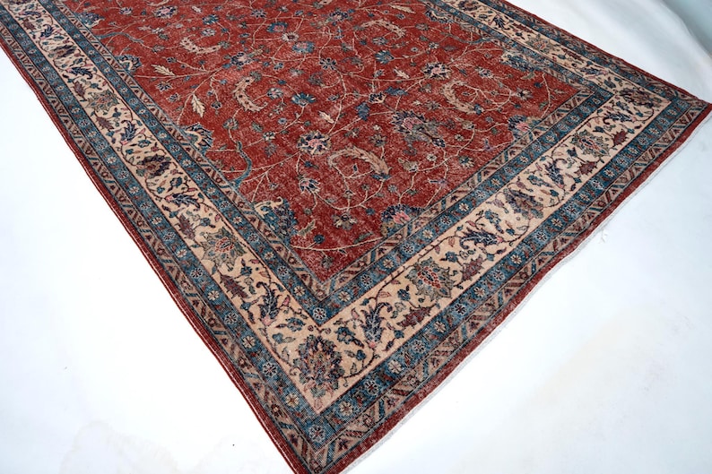 May include: A rectangular, antique-style rug with a red central field and intricate floral patterns. The rug features a border with blue and beige accents, creating a classic and elegant design. The rug's dimensions are not visible.