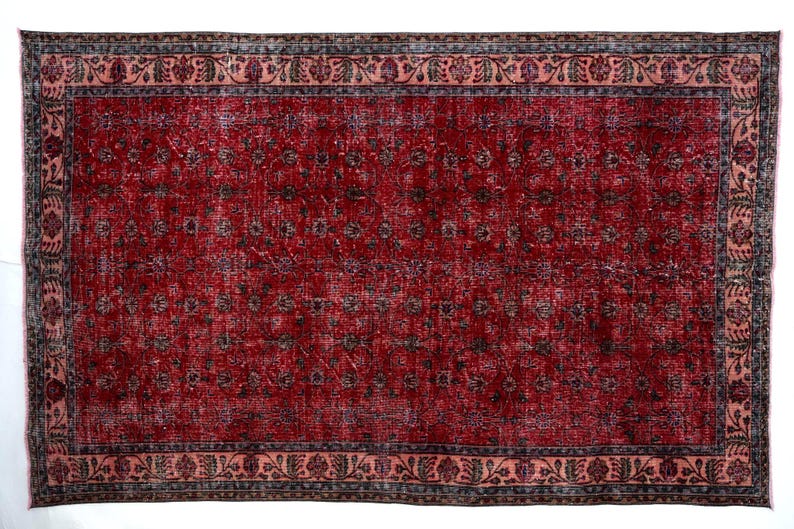 K&ouml;nnte beinhalten: Ein rechteckiger, verwaschen roter Teppich mit floralem Muster. Der Teppich hat ein verblasstes Aussehen, mit einem rosa Rand und einem dunkelgrauen und schwarzen Blumendesign. Der Teppich ist f&uuml;r ein Wohn- oder Schlafzimmer geeignet.