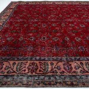 K&ouml;nnte beinhalten: Ein rechteckiger, verwaschen roter Teppich mit einem komplizierten Blumenmuster. Der Teppich hat einen detaillierten Rand mit einer Mischung aus Farben, darunter Rosa, Blau und Braun. Das Design des Teppichs deutet auf einen Vintage- oder Antik-Stil hin, geeignet f&uuml;r die Inneneinrichtung.