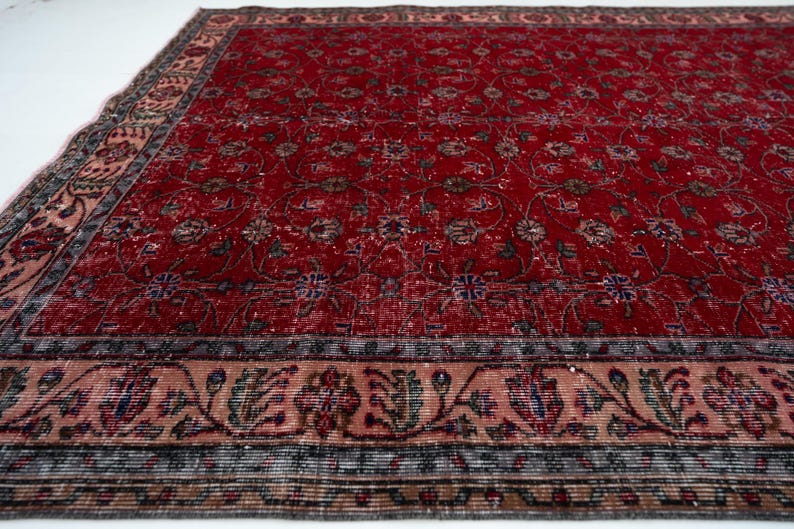 K&ouml;nnte beinhalten: Ein rechteckiger, verwaschen roter Teppich mit einem komplizierten Blumenmuster. Der Teppich hat einen detaillierten Rand mit einer Mischung aus Farben, darunter Rosa, Blau und Braun. Das Design des Teppichs deutet auf einen Vintage- oder Antik-Stil hin, geeignet f&uuml;r die Inneneinrichtung.