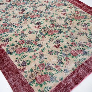 Pode incluir: Um tapete retangular com fundo creme e um padr&atilde;o floral em tons de rosa, azul, verde e roxo. O tapete tem uma borda bord&ocirc; escura, adicionando uma moldura contrastante ao design.