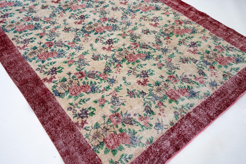 Pode incluir: Um tapete retangular com fundo creme e um padr&atilde;o floral em tons de rosa, azul, verde e roxo. O tapete tem uma borda bord&ocirc; escura, adicionando uma moldura contrastante ao design.