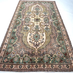 May include: A rectangular area rug featuring a central cream medallion surrounded by intricate floral and geometric patterns in shades of sage green, dusty rose, and dark brown. The border displays a repeating motif of small stars and floral elements.
