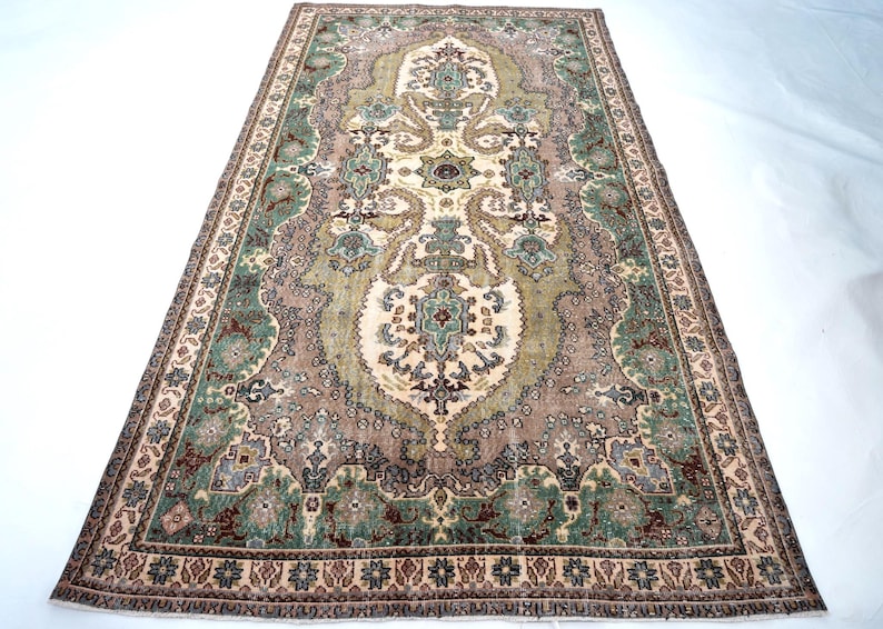 May include: A rectangular area rug featuring a central cream medallion surrounded by intricate floral and geometric patterns in shades of sage green, dusty rose, and dark brown. The border displays a repeating motif of small stars and floral elements.