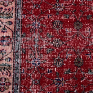 K&ouml;nnte beinhalten: Nahaufnahme eines Abschnitts eines roten Vintage-Teppichs mit floralen Mustern. Der Teppich hat ein rotes Mittelfeld mit verblassten floralen Designs in Blau, Gr&uuml;n und Braun. Ein Rand mit einem rosa-grauen Blumendesign umrahmt den Teppich.