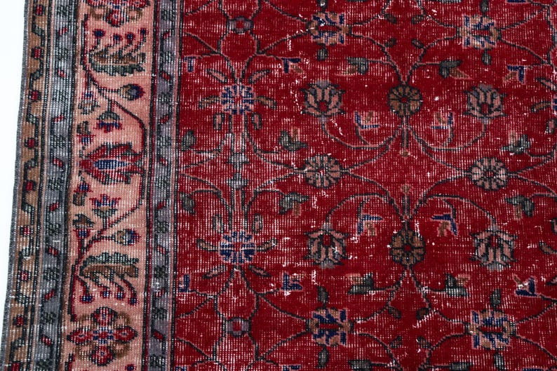 K&ouml;nnte beinhalten: Nahaufnahme eines Abschnitts eines roten Vintage-Teppichs mit floralen Mustern. Der Teppich hat ein rotes Mittelfeld mit verblassten floralen Designs in Blau, Gr&uuml;n und Braun. Ein Rand mit einem rosa-grauen Blumendesign umrahmt den Teppich.