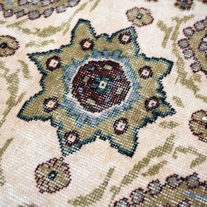 May include: A woven rug featuring a cream-colored background with a repeating pattern of eight-pointed star motifs and circular shapes. The design incorporates shades of olive green, muted blue, and dark brown, showcasing a detailed textile texture.