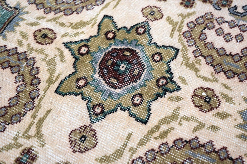 May include: A woven rug featuring a cream-colored background with a repeating pattern of eight-pointed star motifs and circular shapes. The design incorporates shades of olive green, muted blue, and dark brown, showcasing a detailed textile texture.
