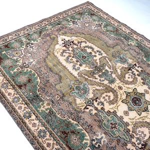May include: A rectangular area rug featuring an intricate central medallion and ornate border patterns in shades of sage green, dusty rose, cream, and dark brown. The woven textile displays symmetrical floral and geometric motifs throughout.