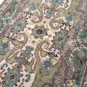 May include: A rectangular area rug featuring an intricate pattern of paisley and floral motifs in shades of sage green, muted brown, cream, and dark red. The design includes a central medallion and a detailed border with repeating geometric shapes.